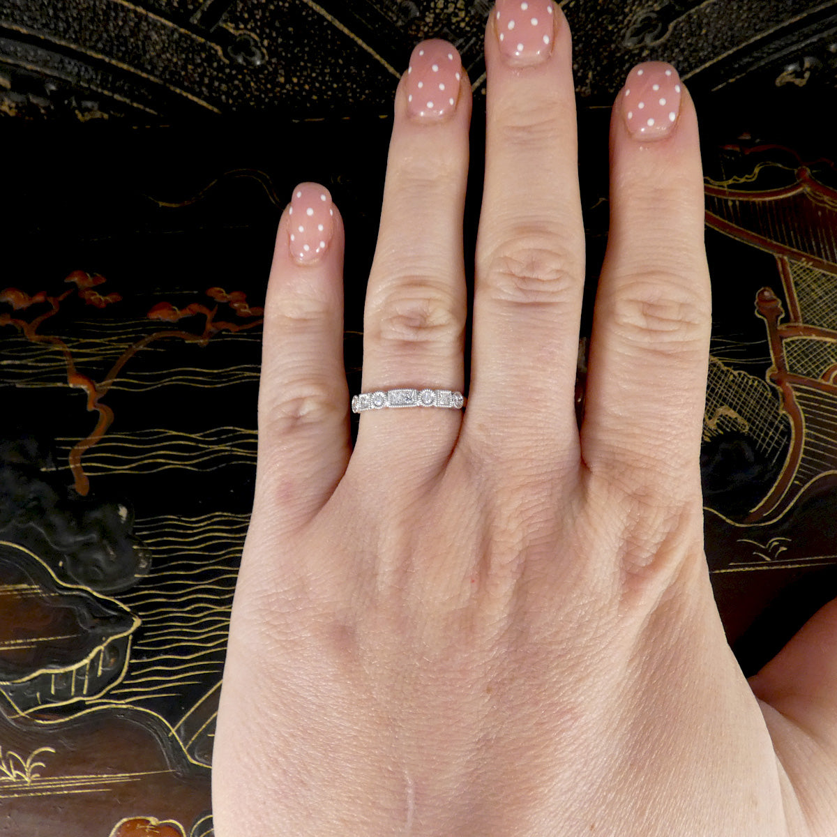 Hand wearing a diamond ring with a decorative background