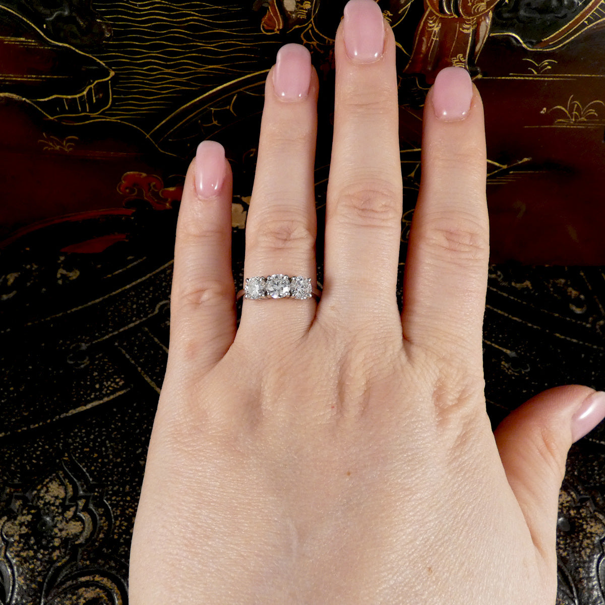 Hand wearing a diamond three stone ring on a decorative background
