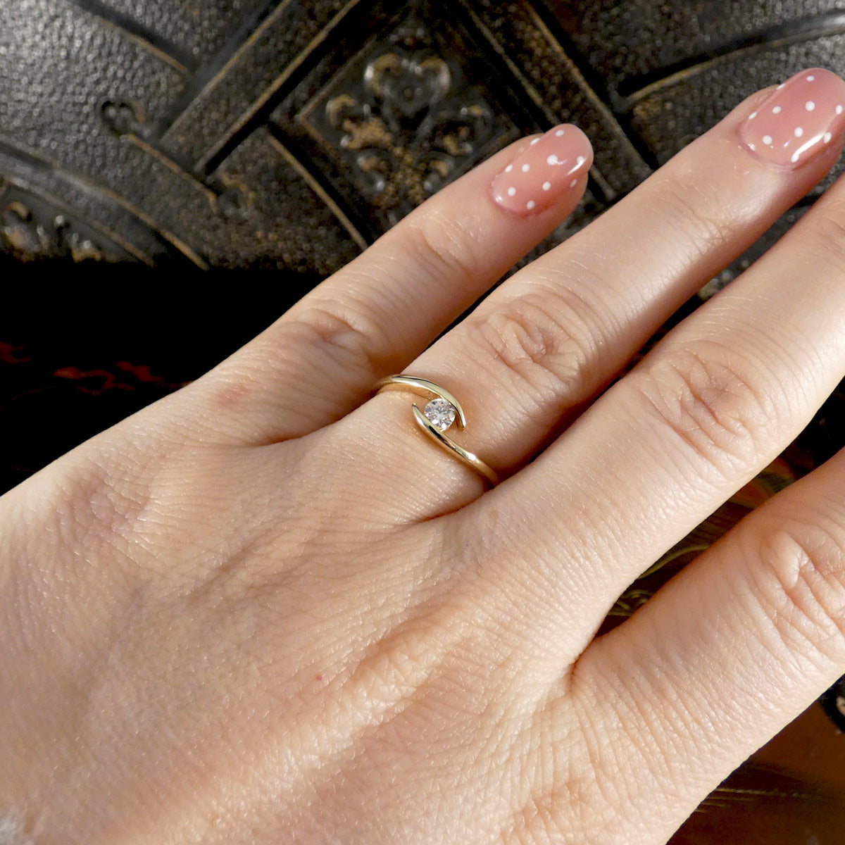 Hand wearing a gold ring with a diamond on a dark textured background