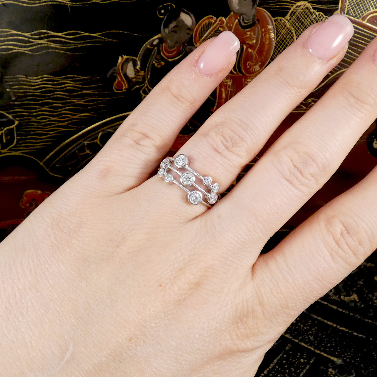 Hand wearing a platinum ring with multiple diamonds on a decorative background