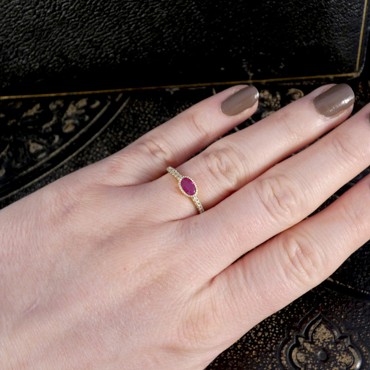 Hand wearing a gold ring with a red gemstone on a dark textured background