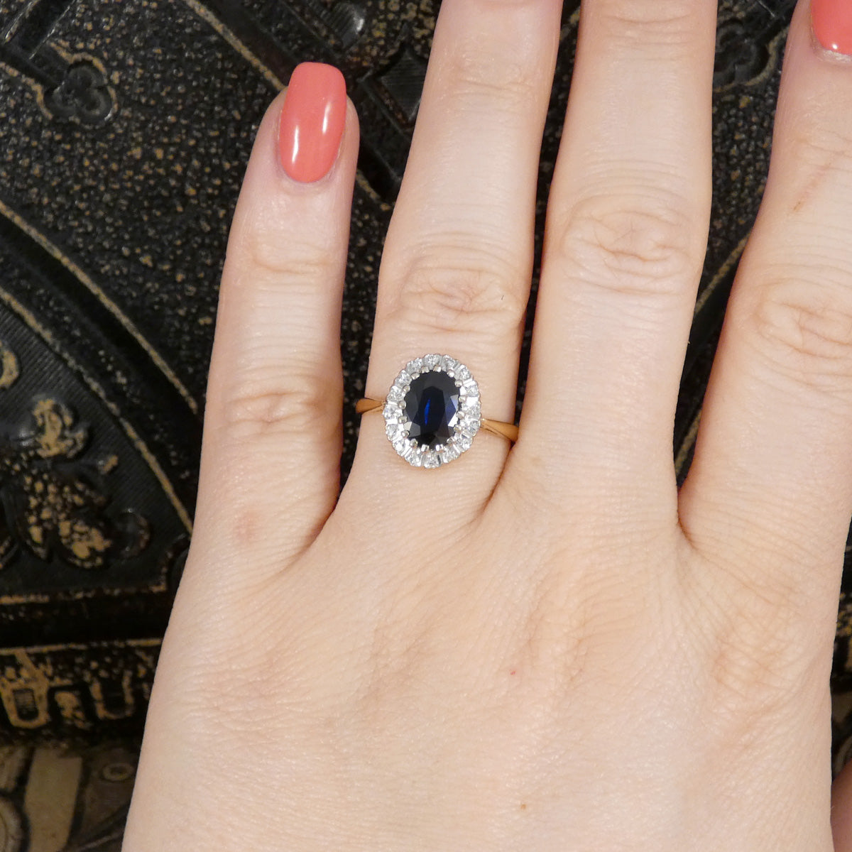 Hand wearing a ring with a blue gemstone and diamond halo on a textured surface
