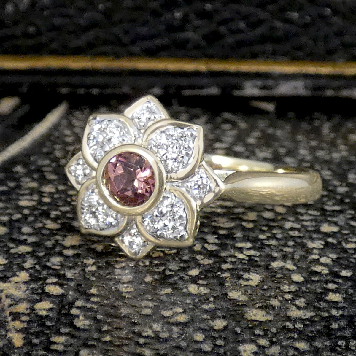 Gold ring with a pink gemstone and diamond accents on a textured surface