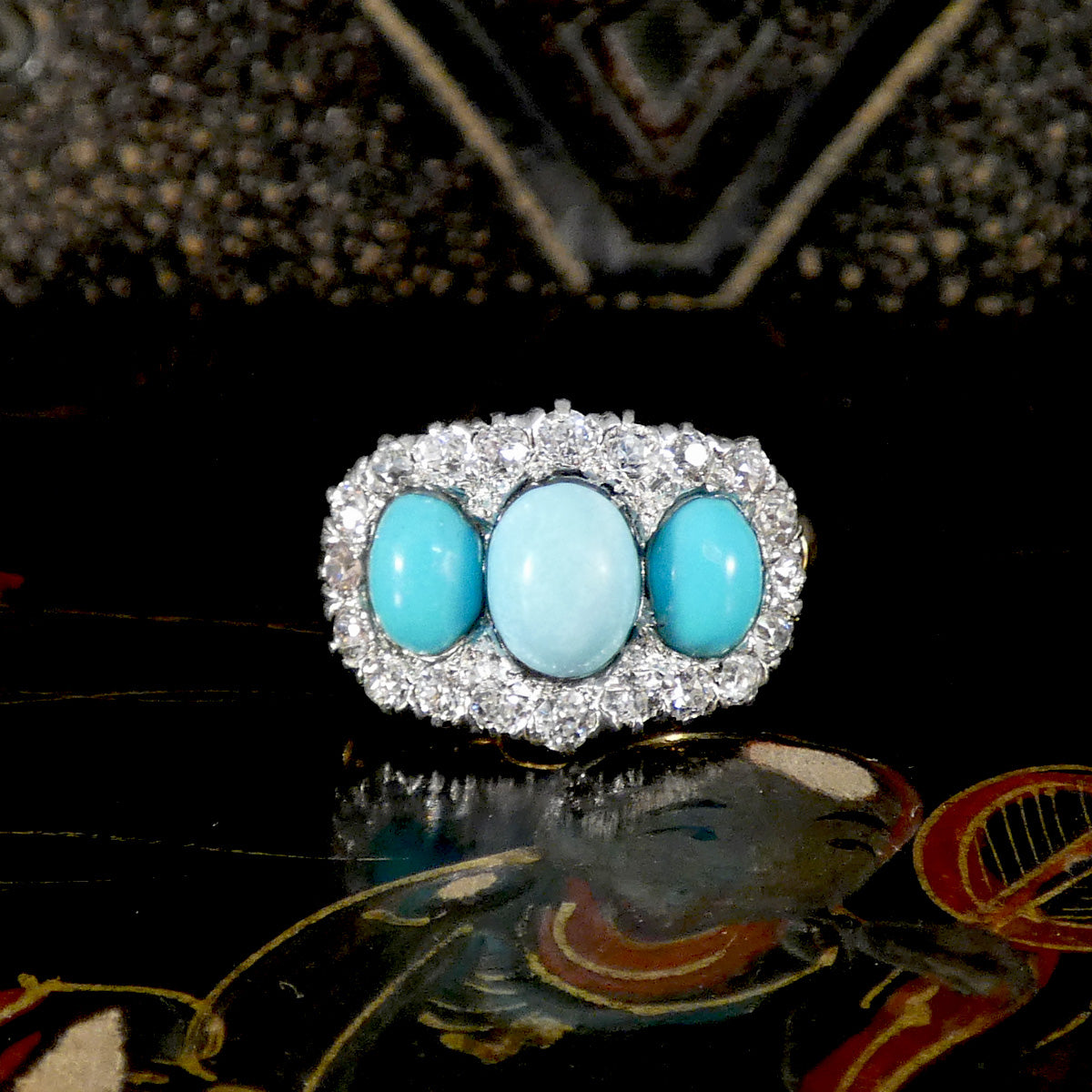 Ring with three turquoise stones and diamonds on a reflective surface