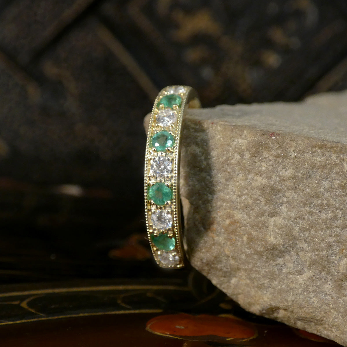 Gold ring with emeralds and diamonds on a stone surface