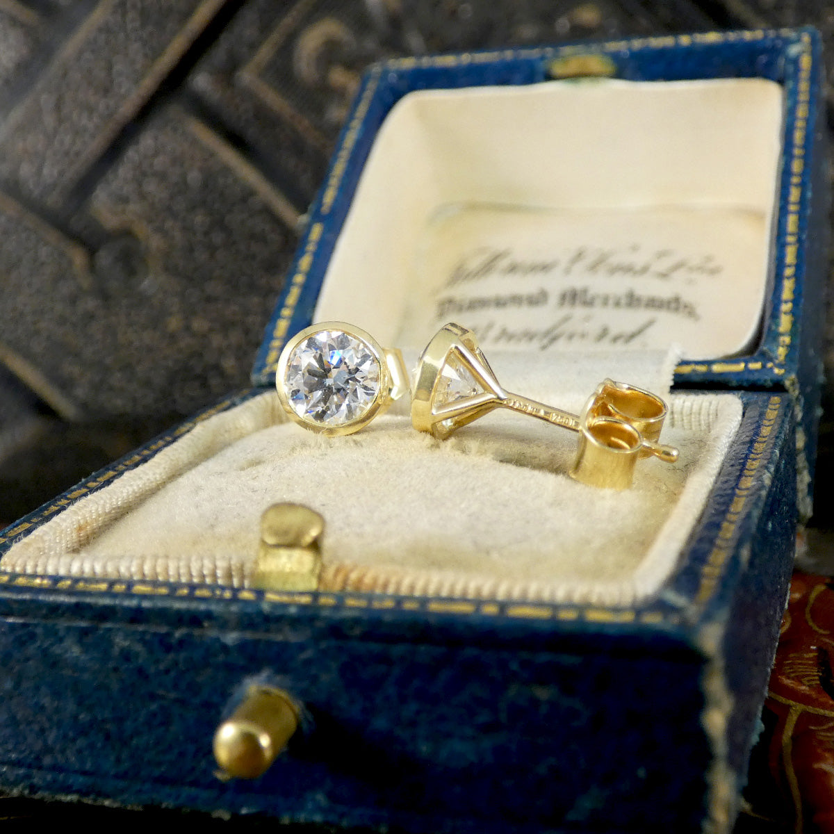 A pair of vintage yellow gold stud earrings with round clear gemstones, displayed inside an open antique blue velvet jewelry box with gold trim.