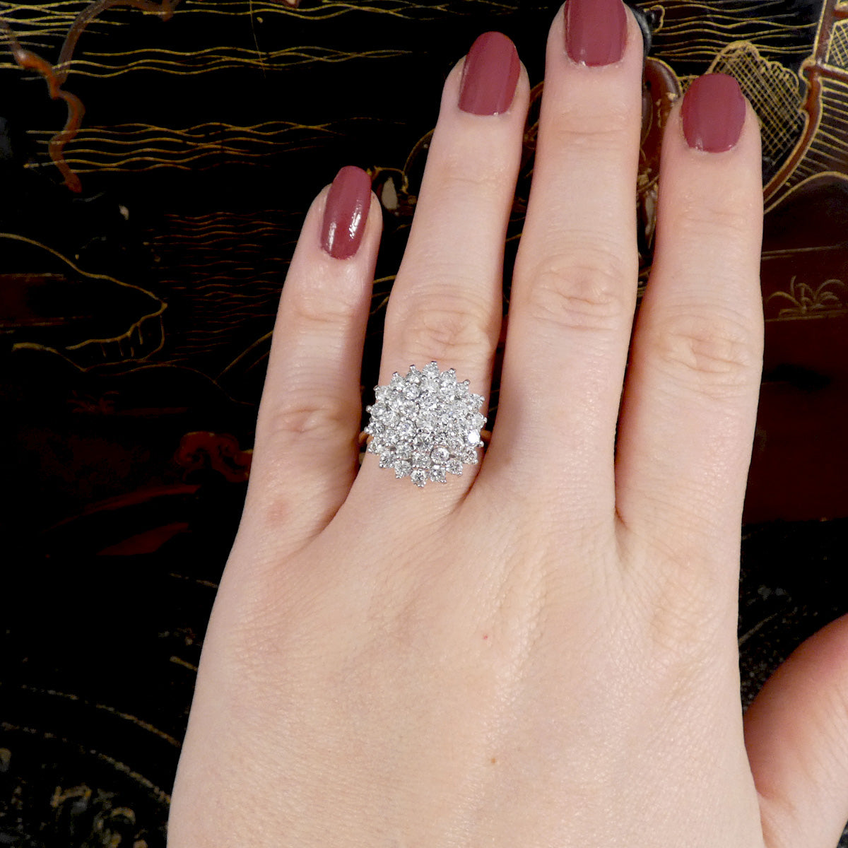 Hand wearing a silver ring with a diamond cluster on a decorative background