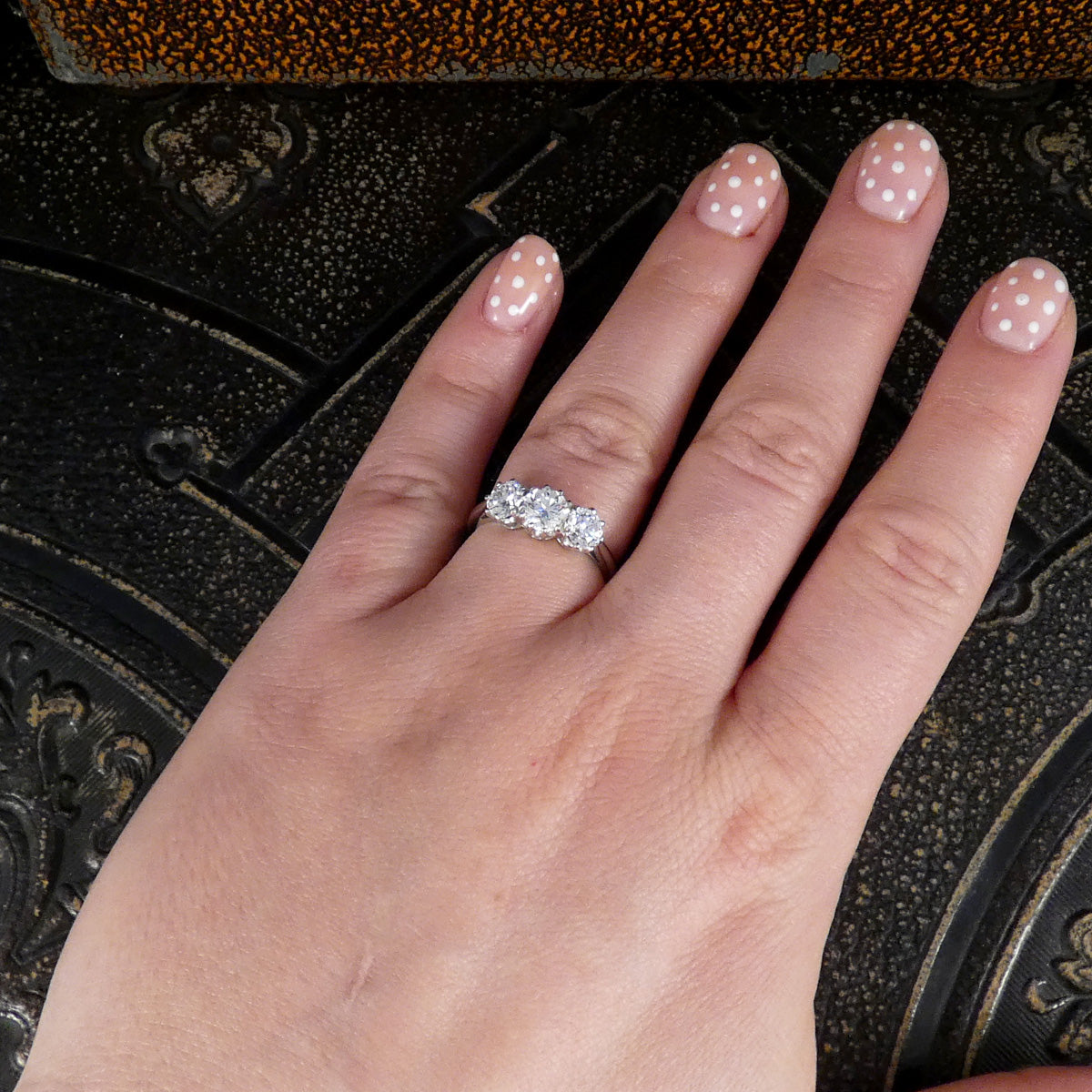 Hand wearing a diamond ring with polka dot nail polish on a dark textured background