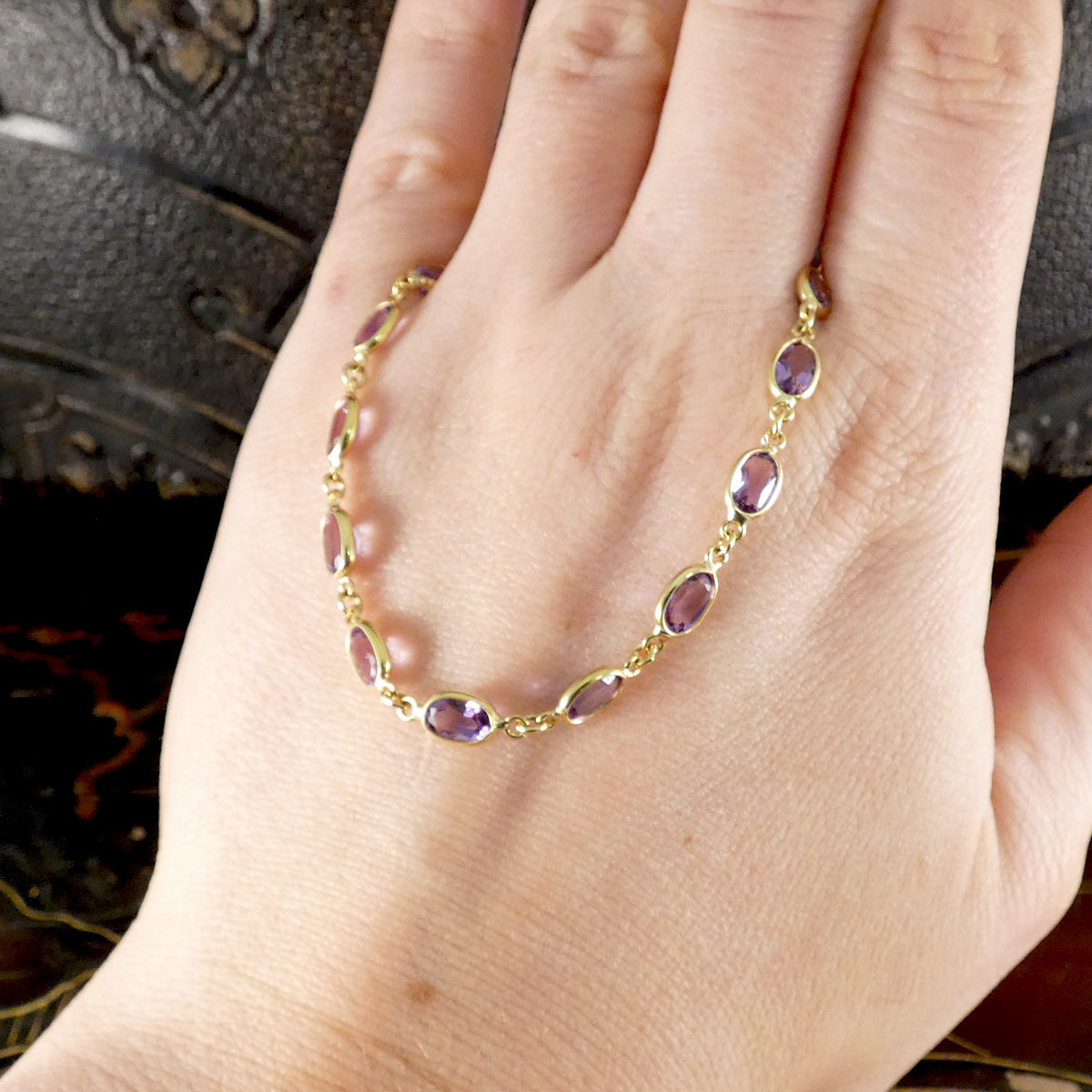 Gold bracelet with purple stones on a hand against a dark background