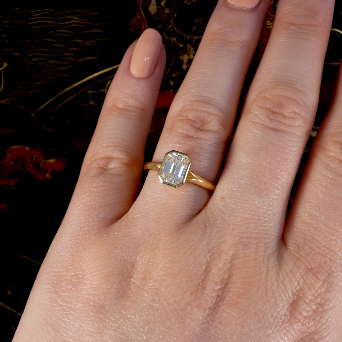 The perfect modern engagement ring shown on the finger, 1.55ct Emerald Cut Diamond Solitaire in a Bezel Setting in 18ct Yellow Gold, showcasing a clear and bright diamond graded F/VS