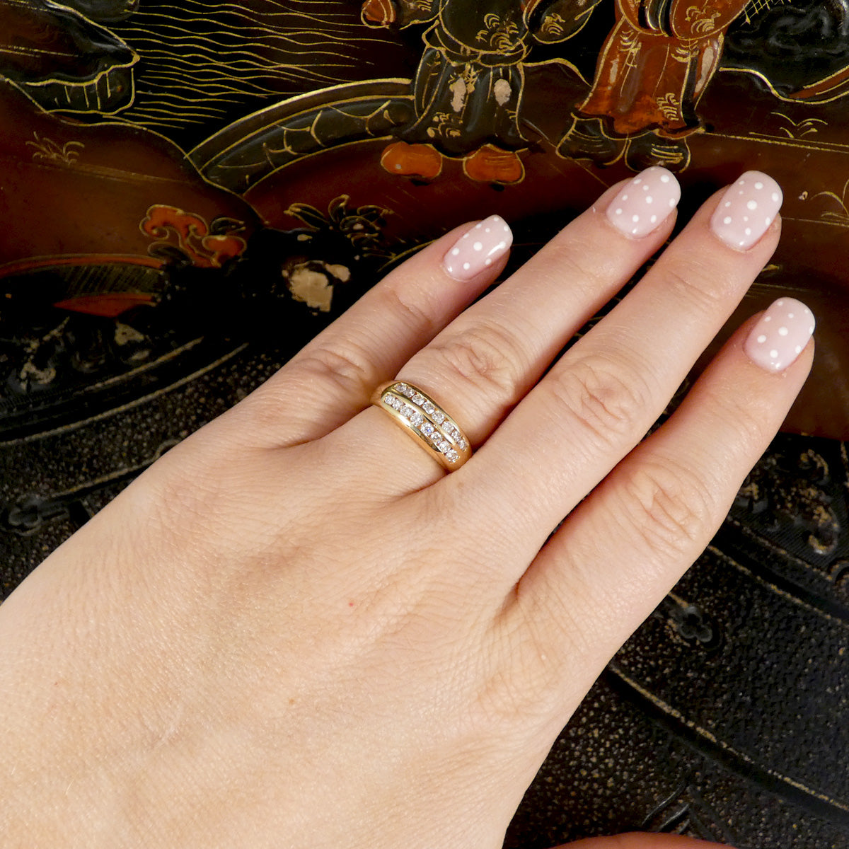 A channel set diamond double row ring in yellow gold displayed on the had with a dark background