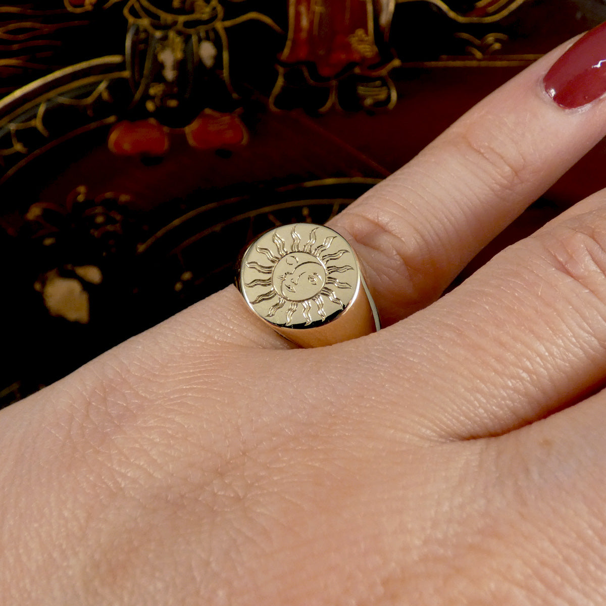 A solid yellow gold signet ring with a face engraved with a sun and moon shown on the pinky finger.