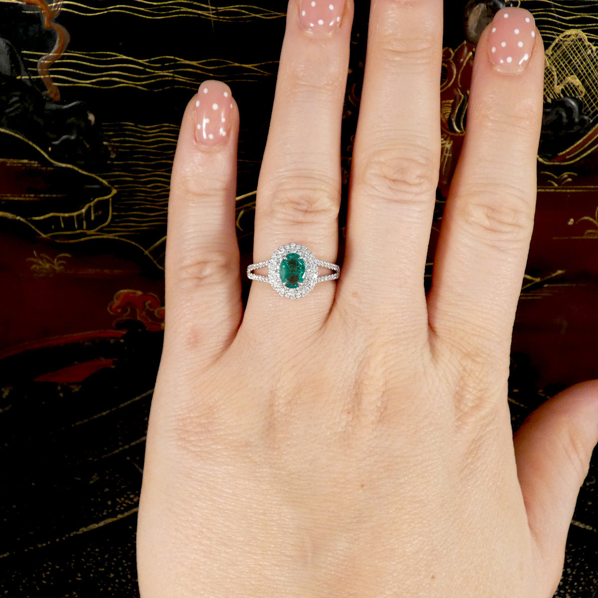 Hand wearing a ring with an emerald stone on a decorative background