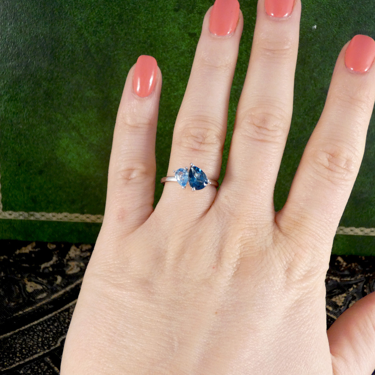 Hand wearing a ring with a blue gemstone on a green background