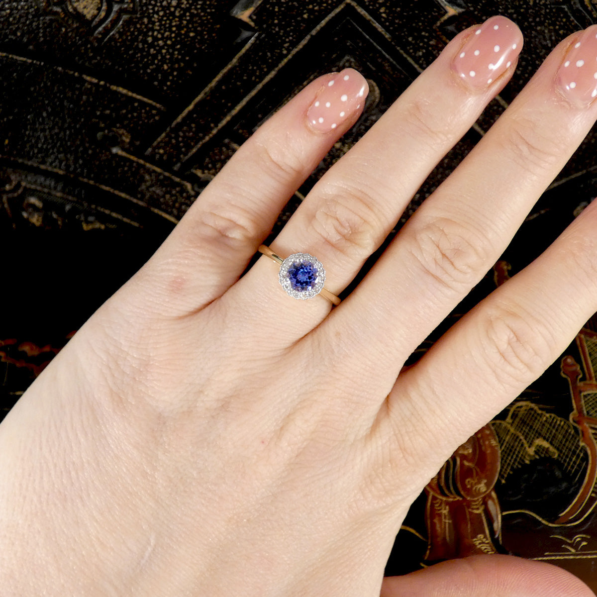 Hand wearing a ring with a blue gemstone on a decorative background