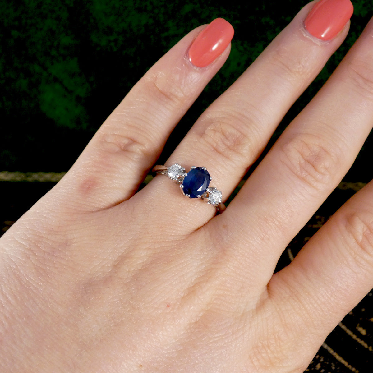 Hand wearing a ring with a blue sapphire gemstone on a blurred natural background