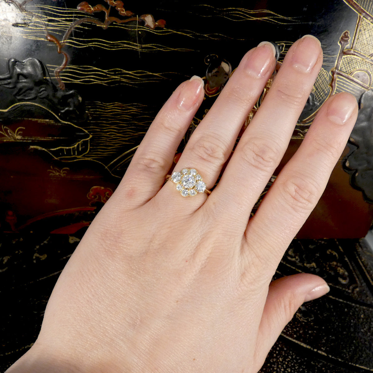 Hand wearing a diamond ring with an ornate background