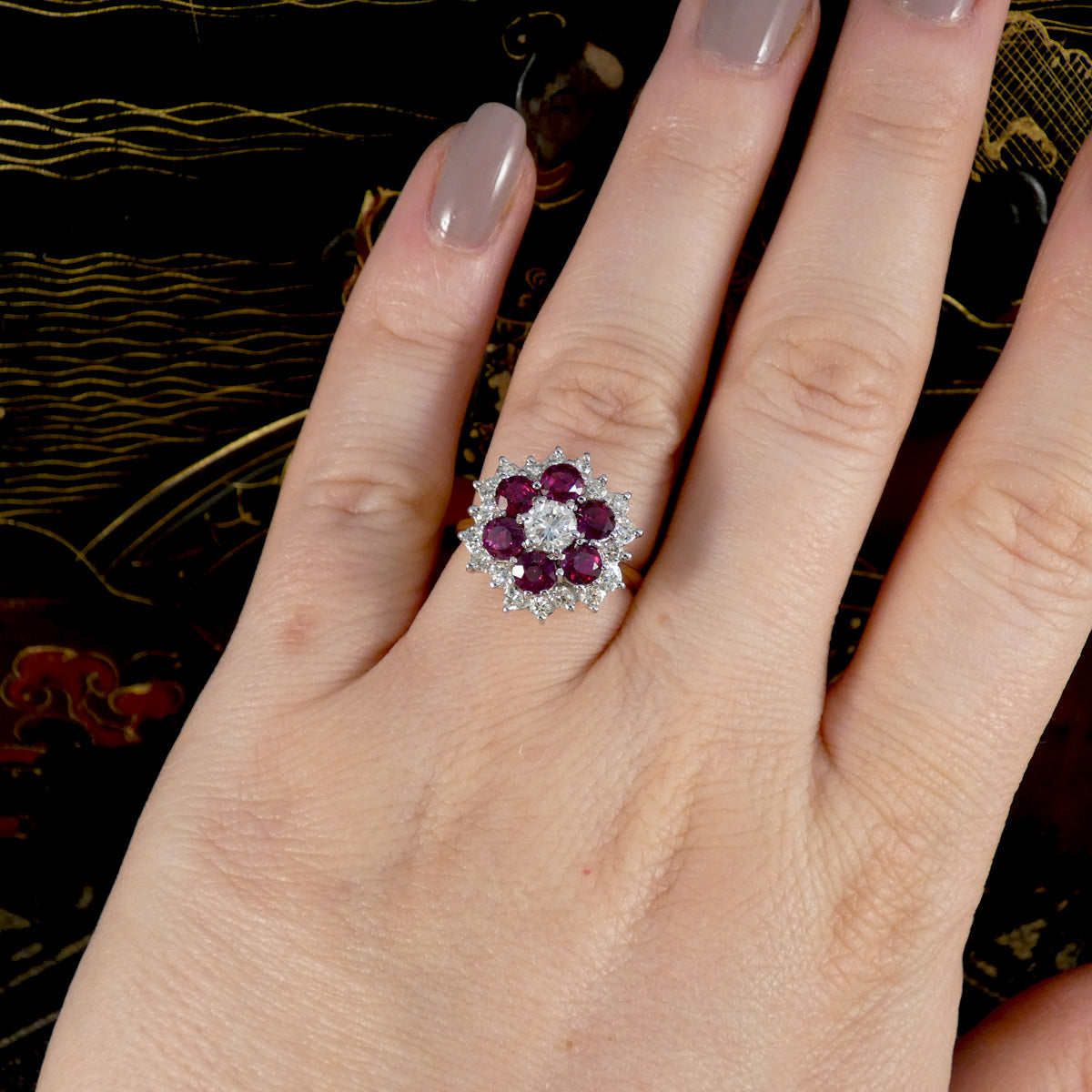 Hand wearing a ring with red gemstones on a decorative background
