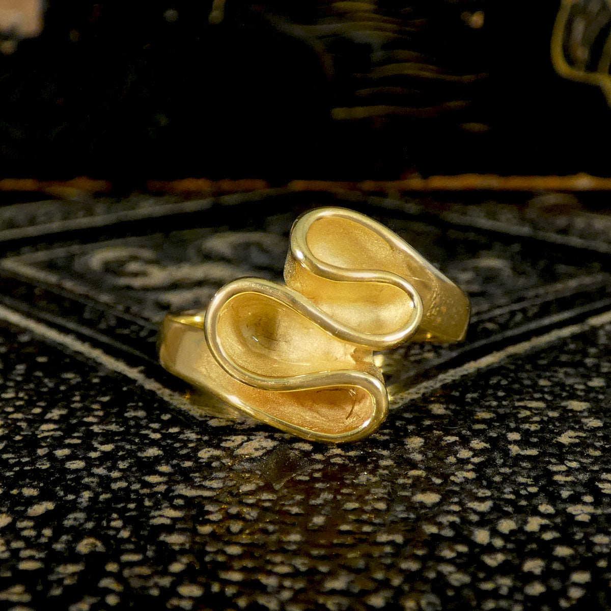 Solid Gold ribbon ring with a unique design on a textured black surface
