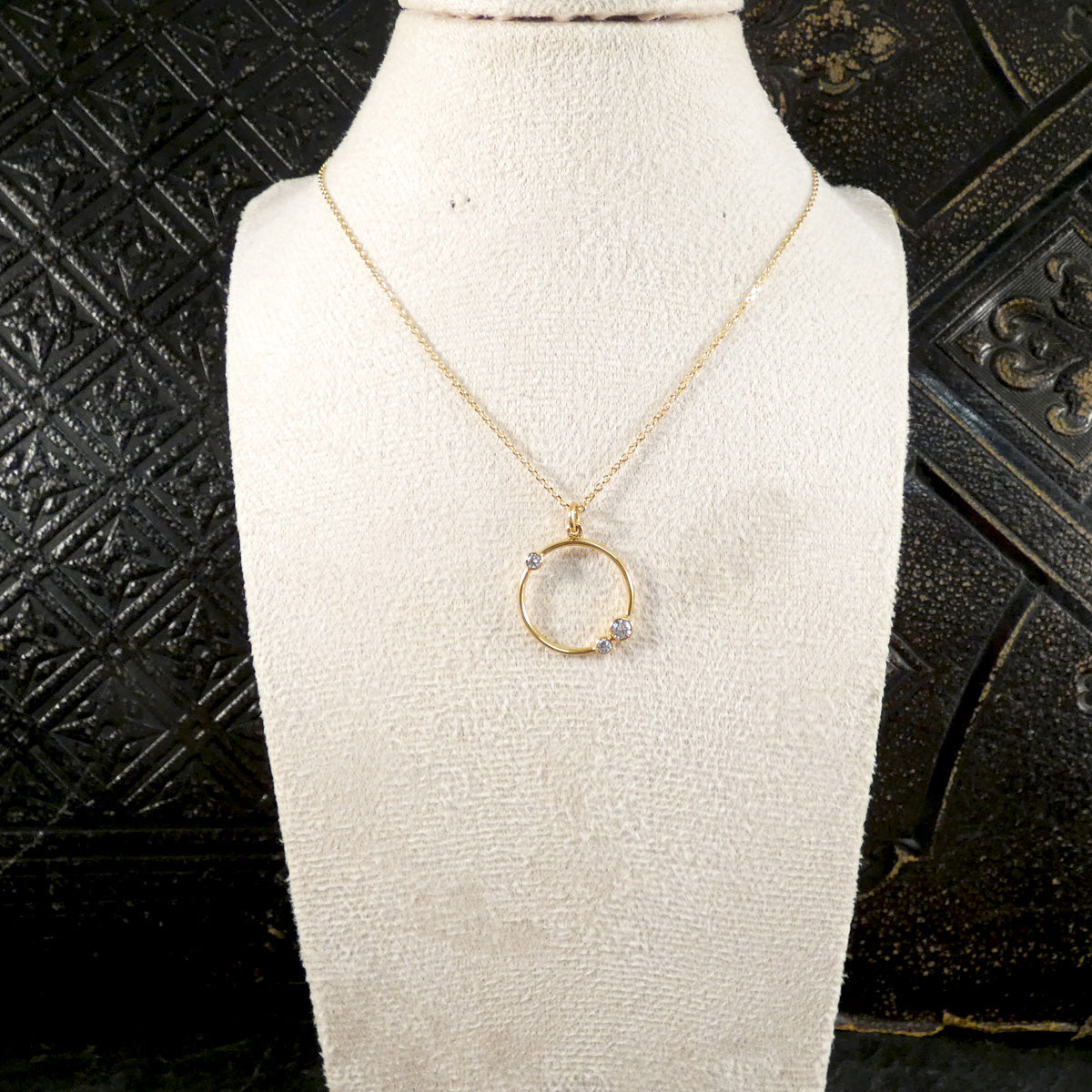Gold necklace with a circular pendant on a white mannequin bust against a textured black background