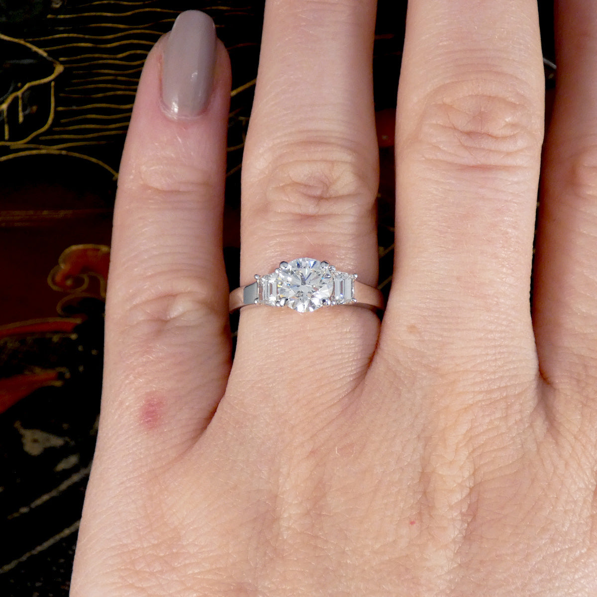 A brilliant cut and trapezoid cut Diamond three stone ring shown on the ring finger on the hand.