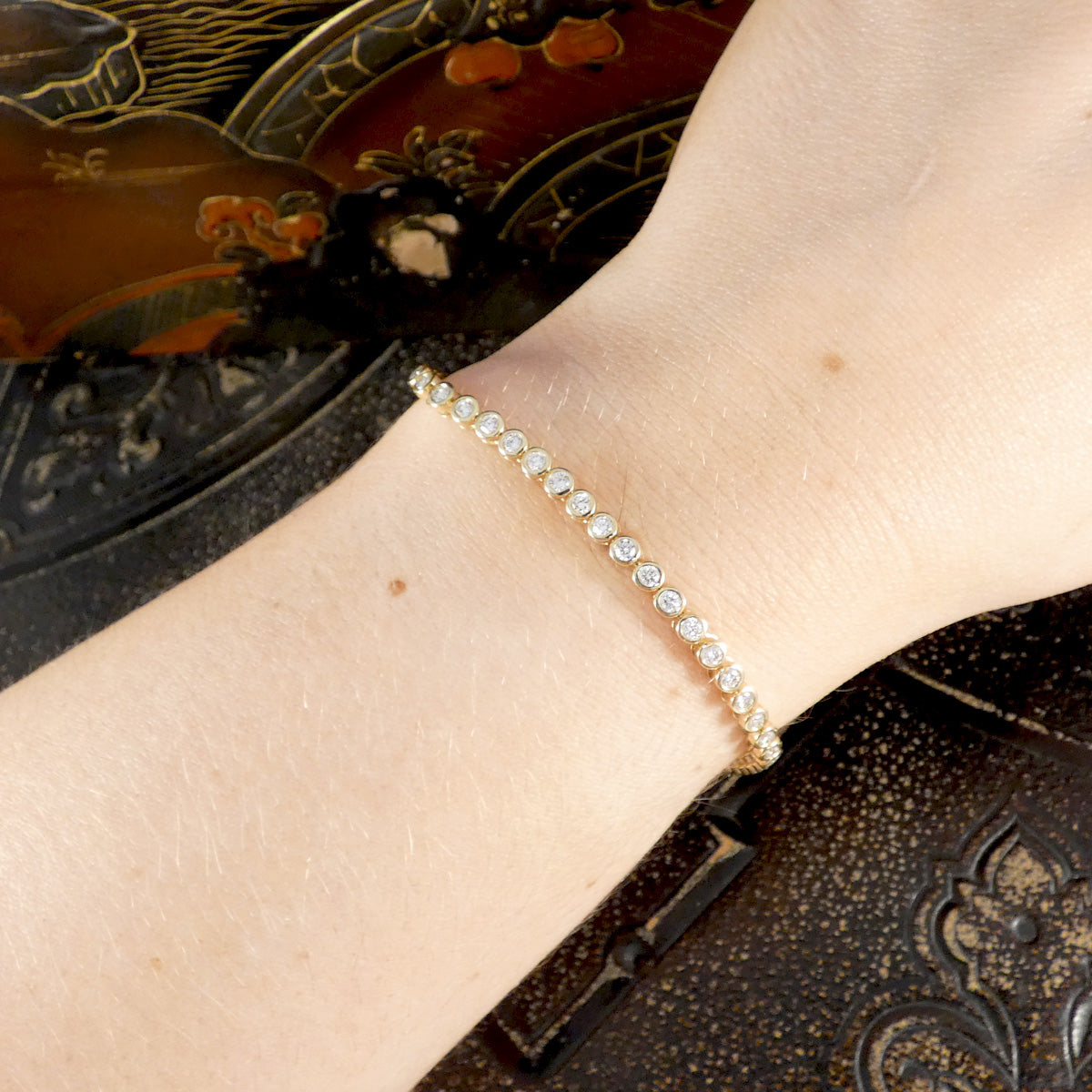 Gold bracelet with diamond on a wrist against an ornate background