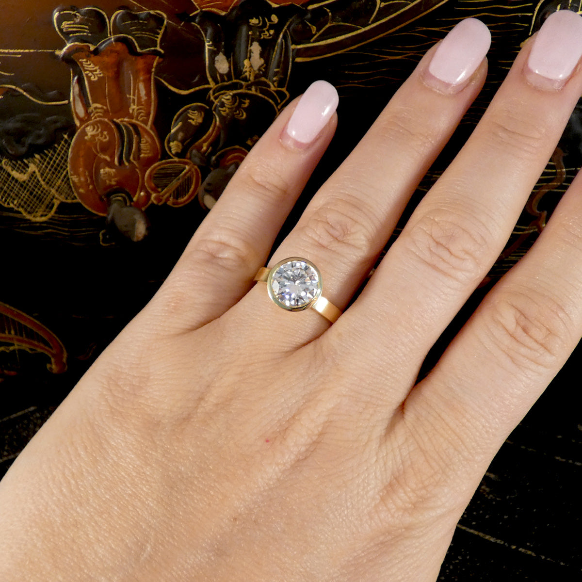 A large diamond solitaire ring in a rub over bezel setting in 18ct yellow gold shown on the hand on the wedding finger.