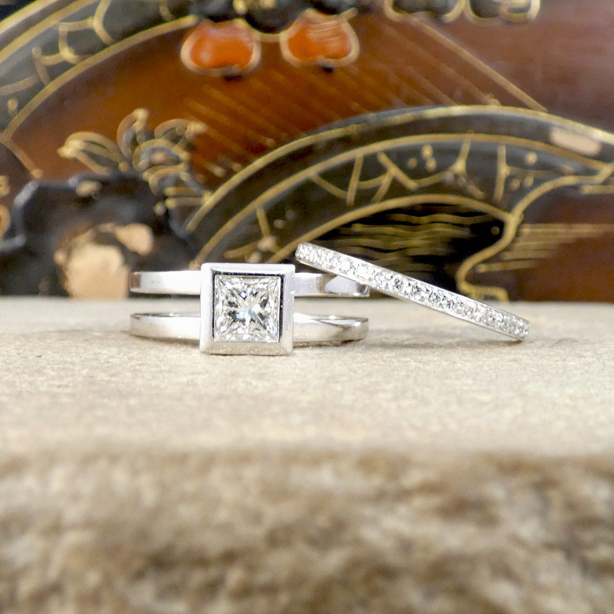 Two diamond rings on a textured surface with an ornate object in the background
