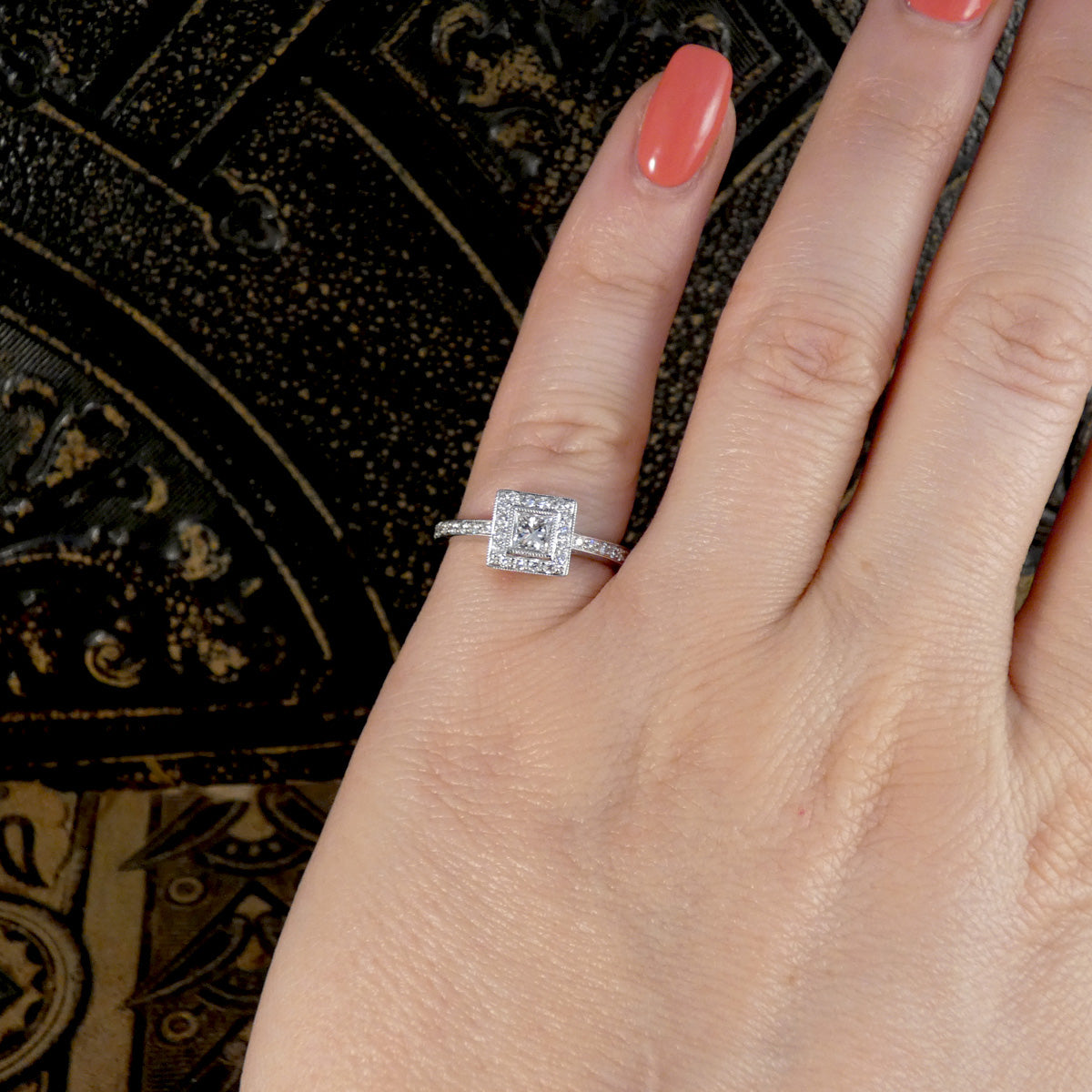 Hand wearing a diamond ring with a decorative background