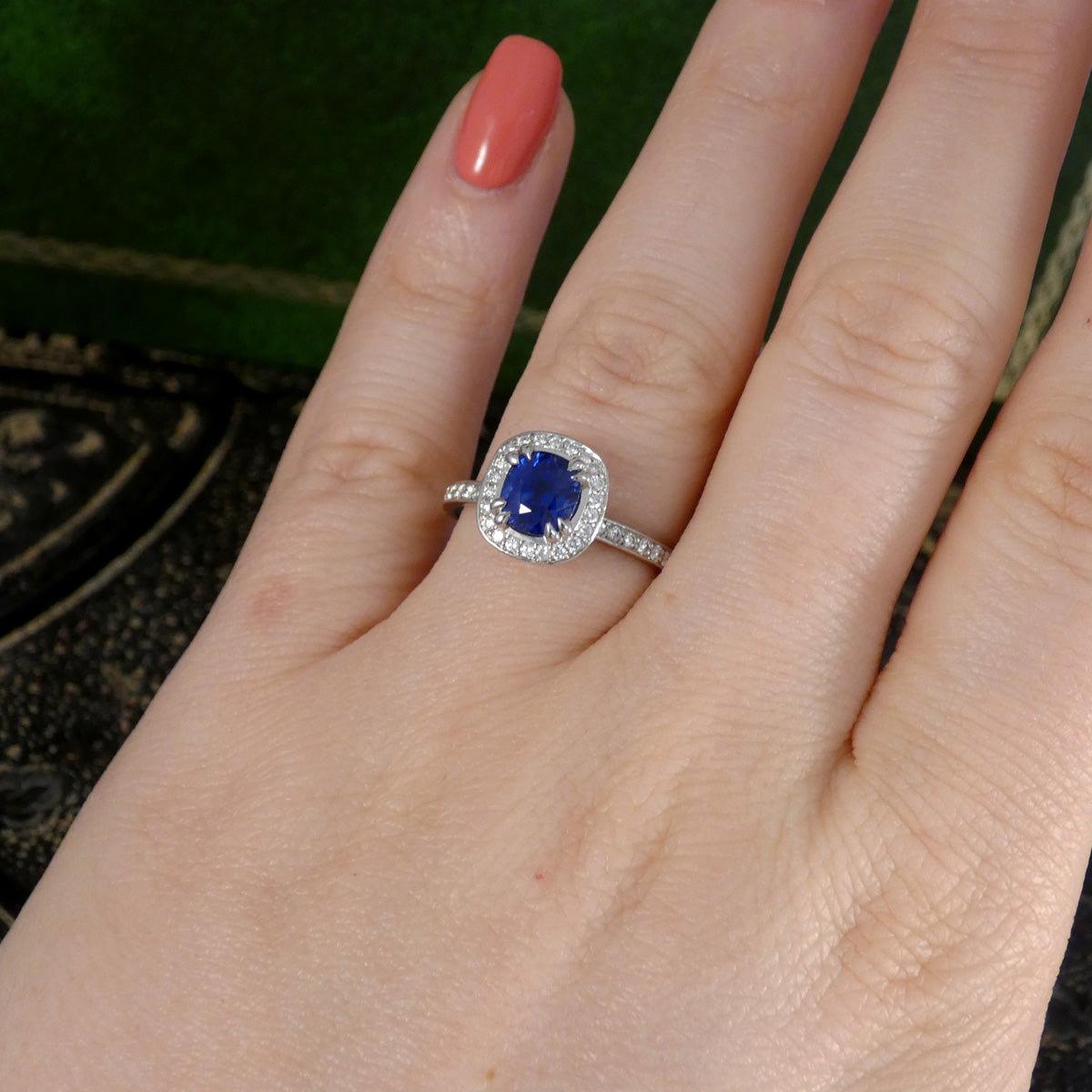 Hand wearing a ring with a blue sapphire gemstone and diamond accents against a blurred background