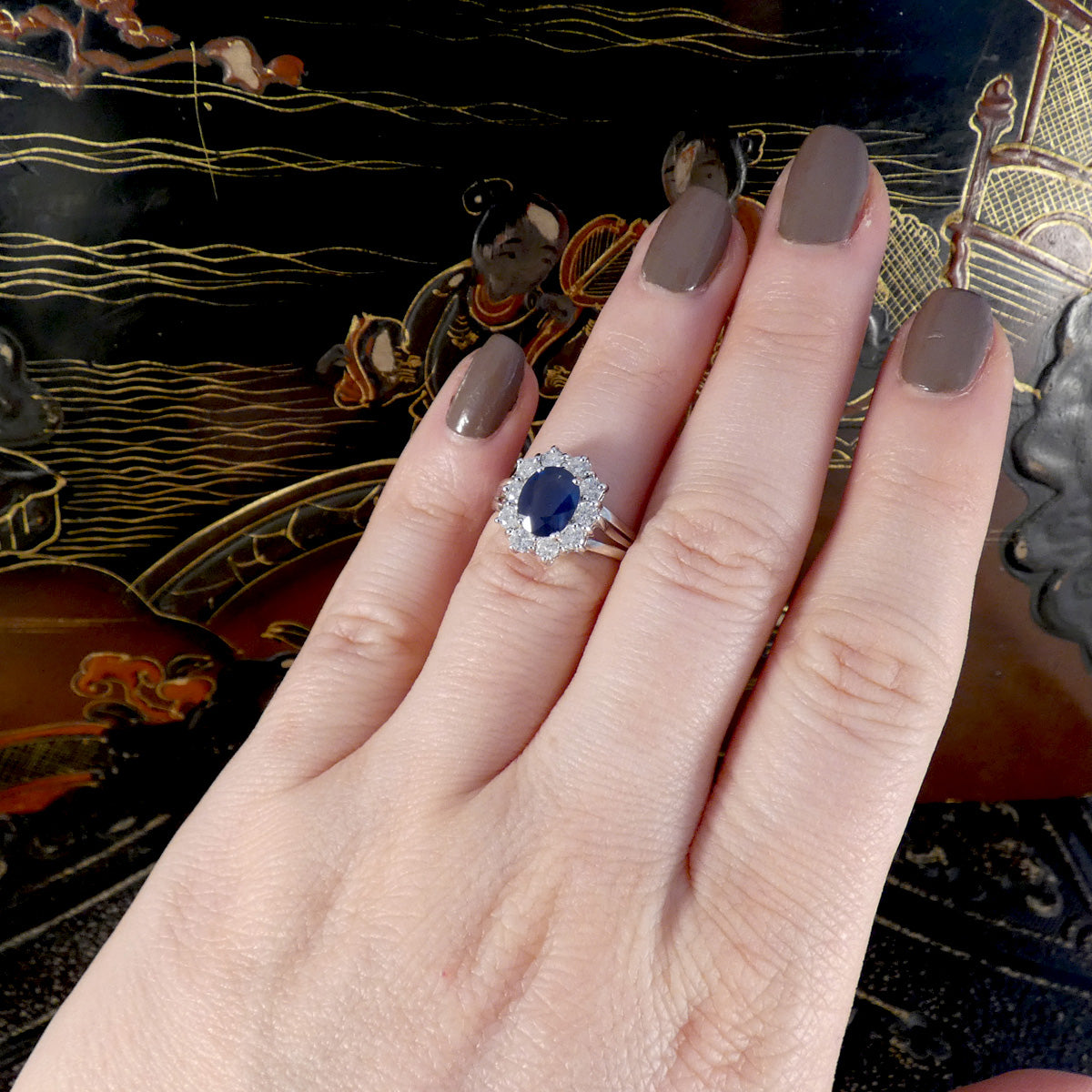 Hand wearing a ring with a blue gemstone against an ornate background