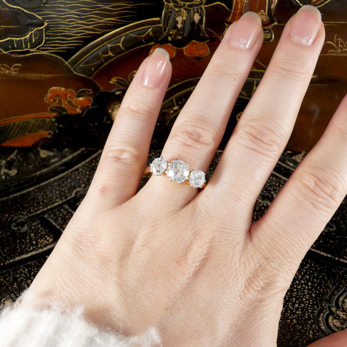Hand wearing a diamond three stone ring with an ornate background
