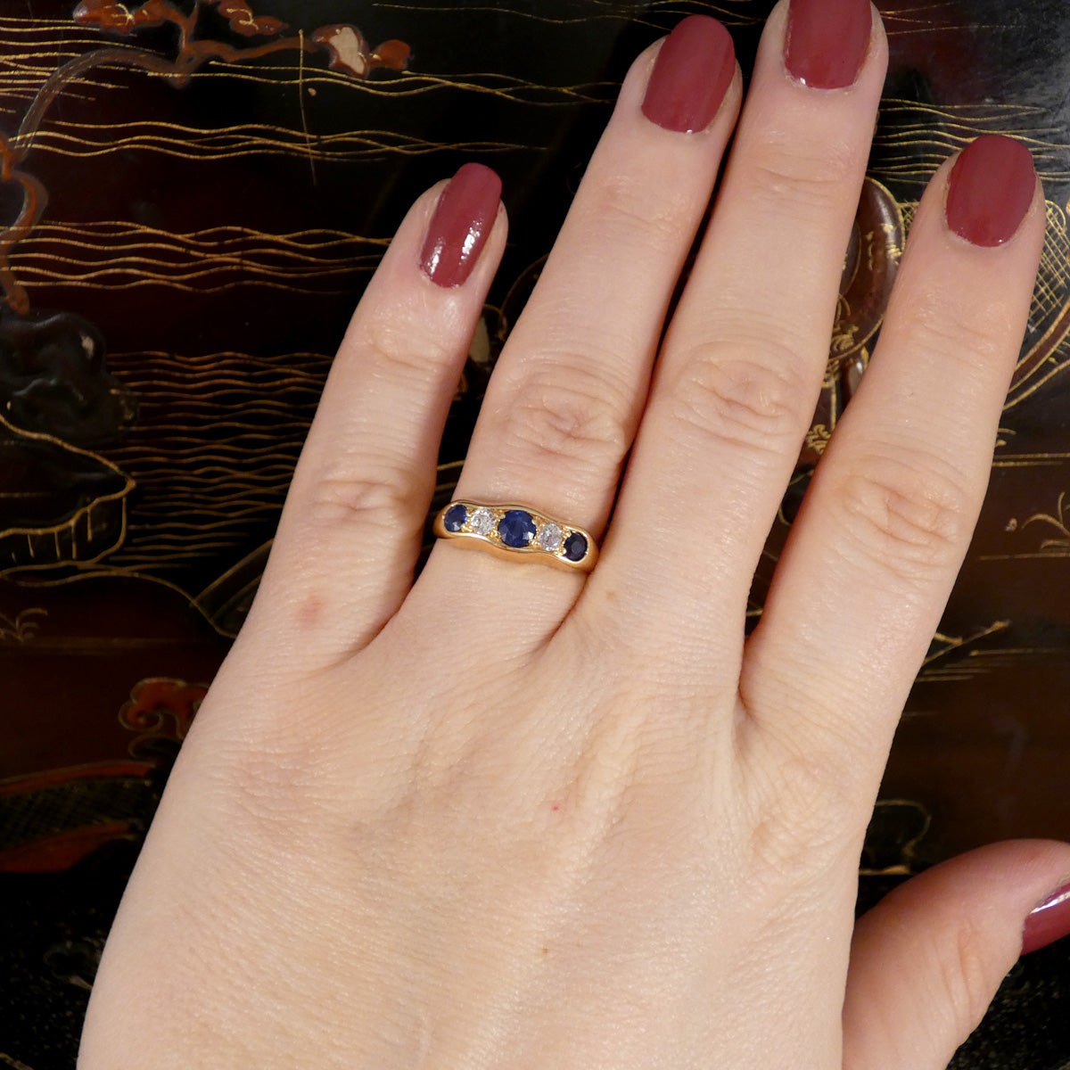 A sapphire and diamond five stone ring in gold shown on the hand.