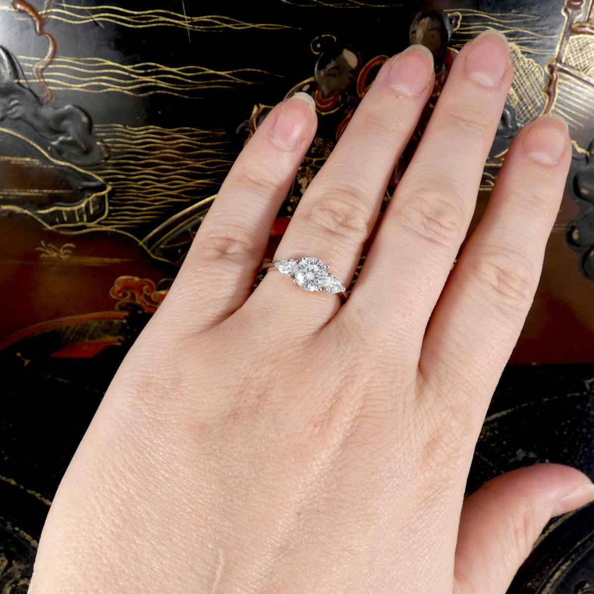 Hand wearing a diamond engagement ring with a decorative background