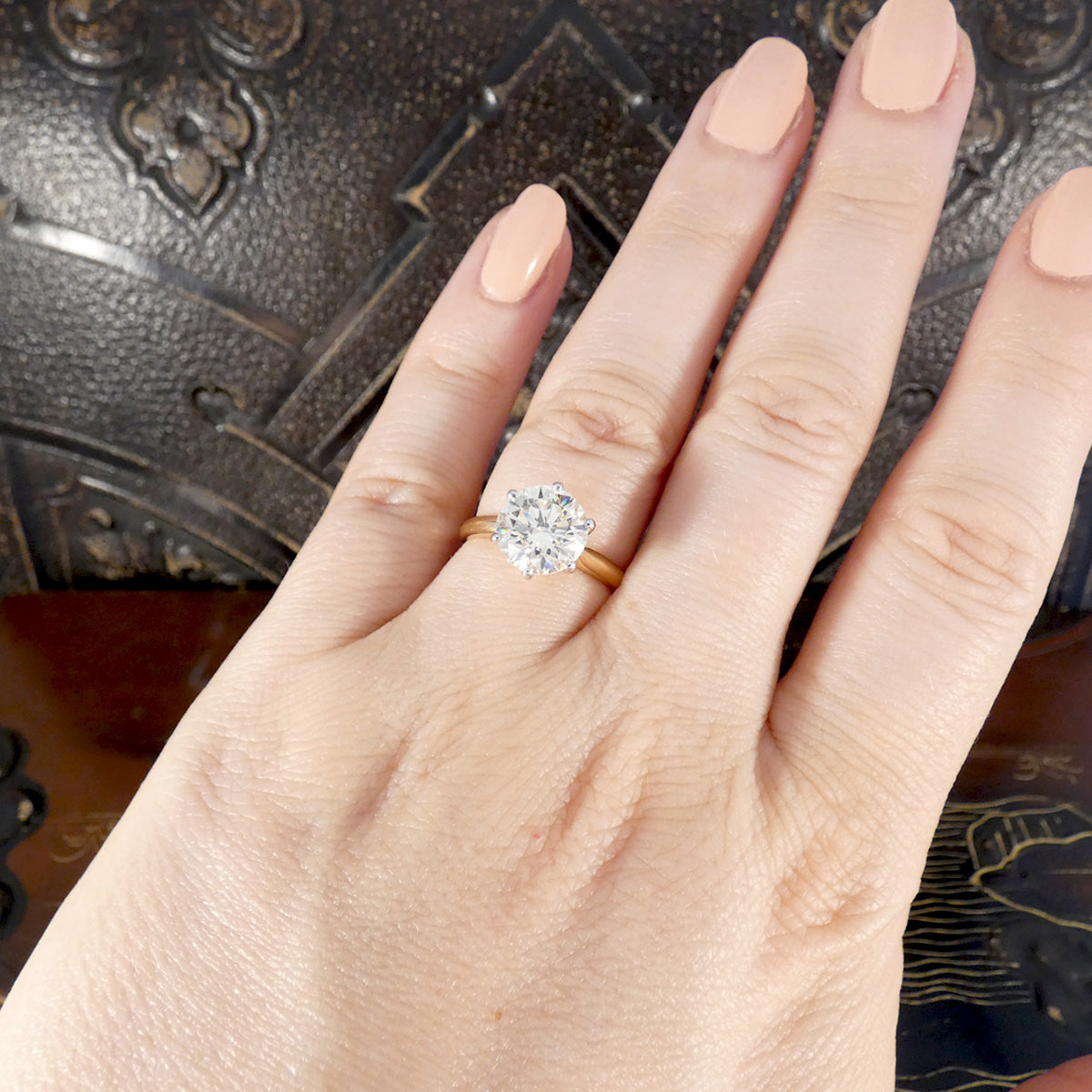 Hand wearing a diamond ring with an ornate background
