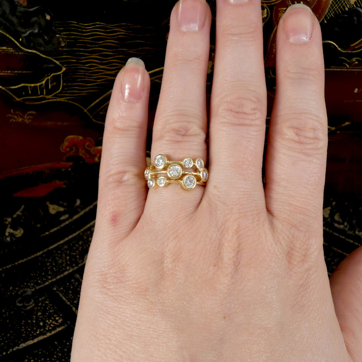 Hand wearing a gold bubble style ring with diamonds on a decorative background