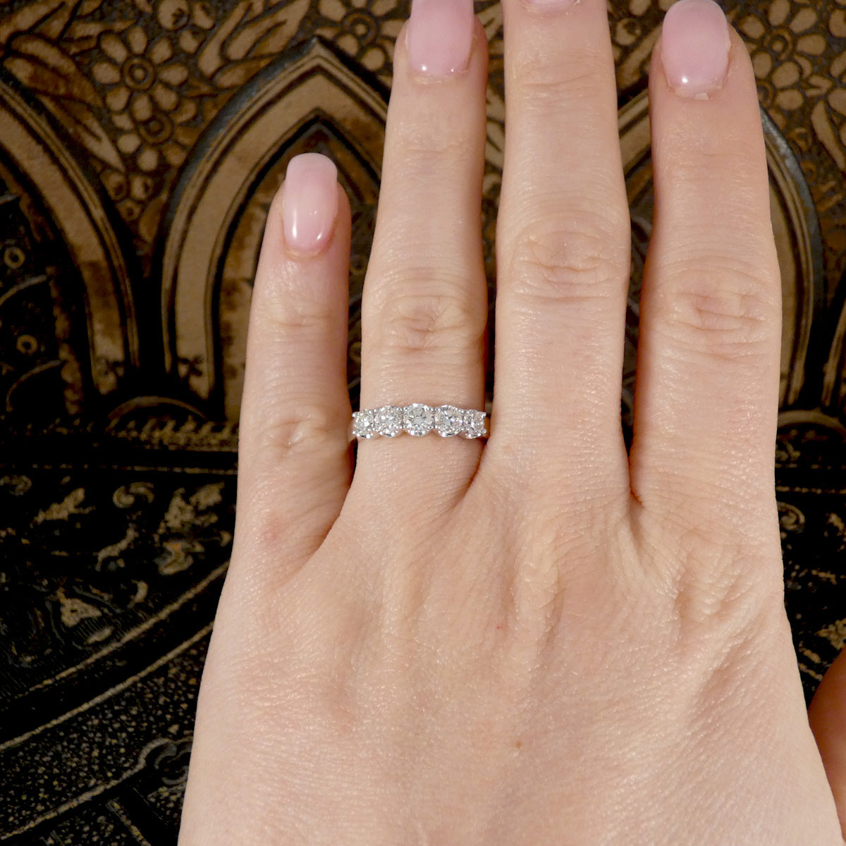 Hand wearing a diamond ring with a decorative background