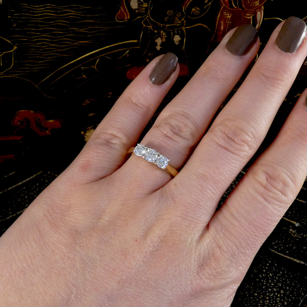 Hand wearing a diamond ring with a dark, decorative background