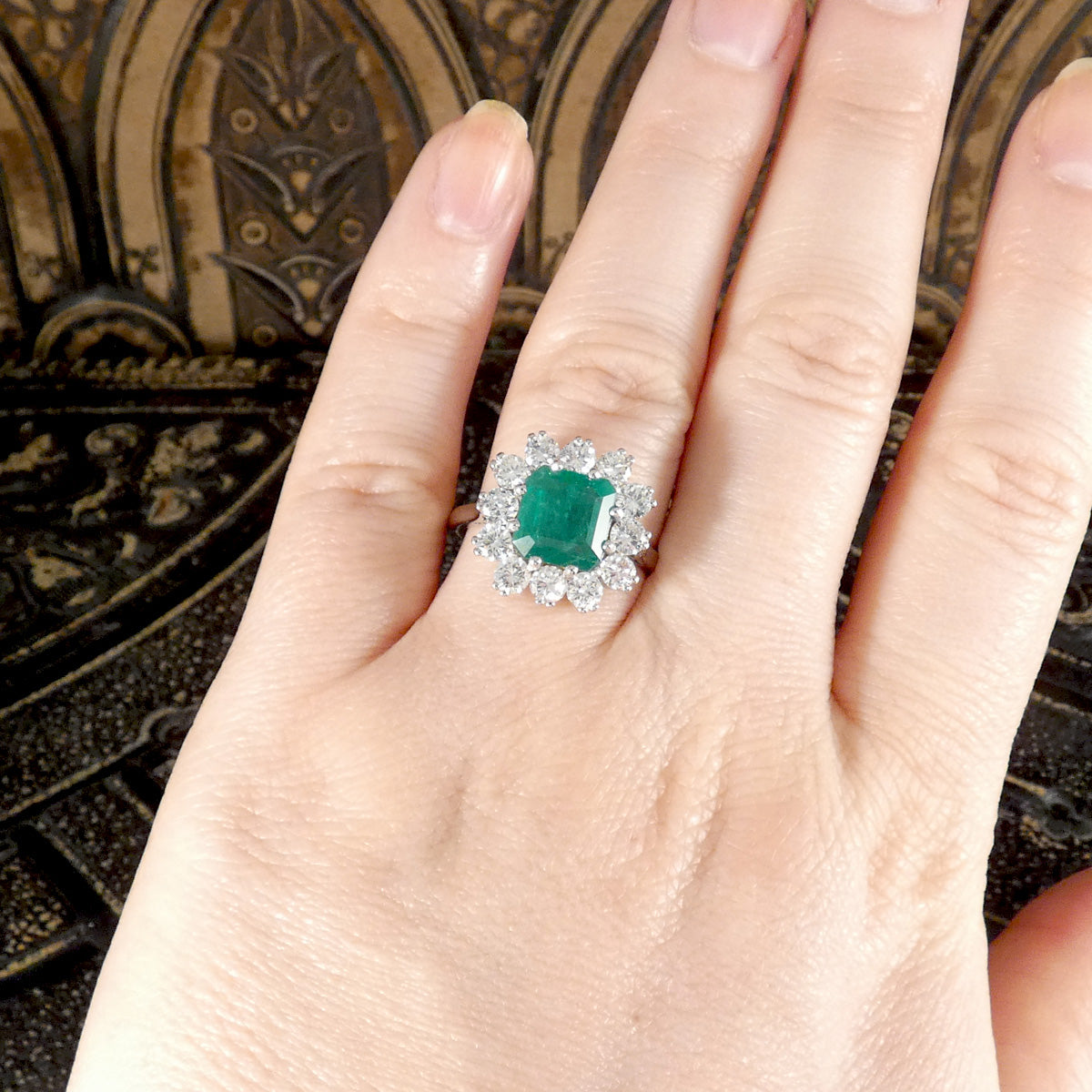 A gorgeous Emerald and Diamond cluster ring shown on the hand to see the size ratio and reference. 
