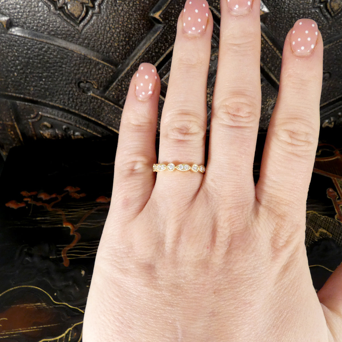Hand wearing a gold ring with small stones against a decorative background