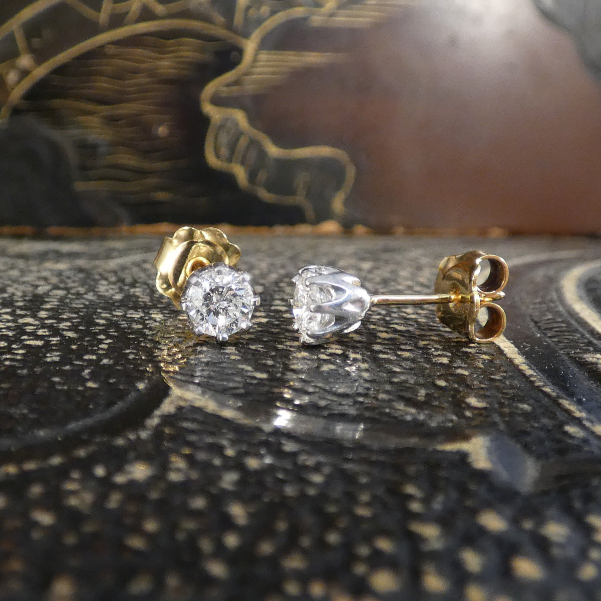 Diamond stud earrings on a textured surface with a blurred background