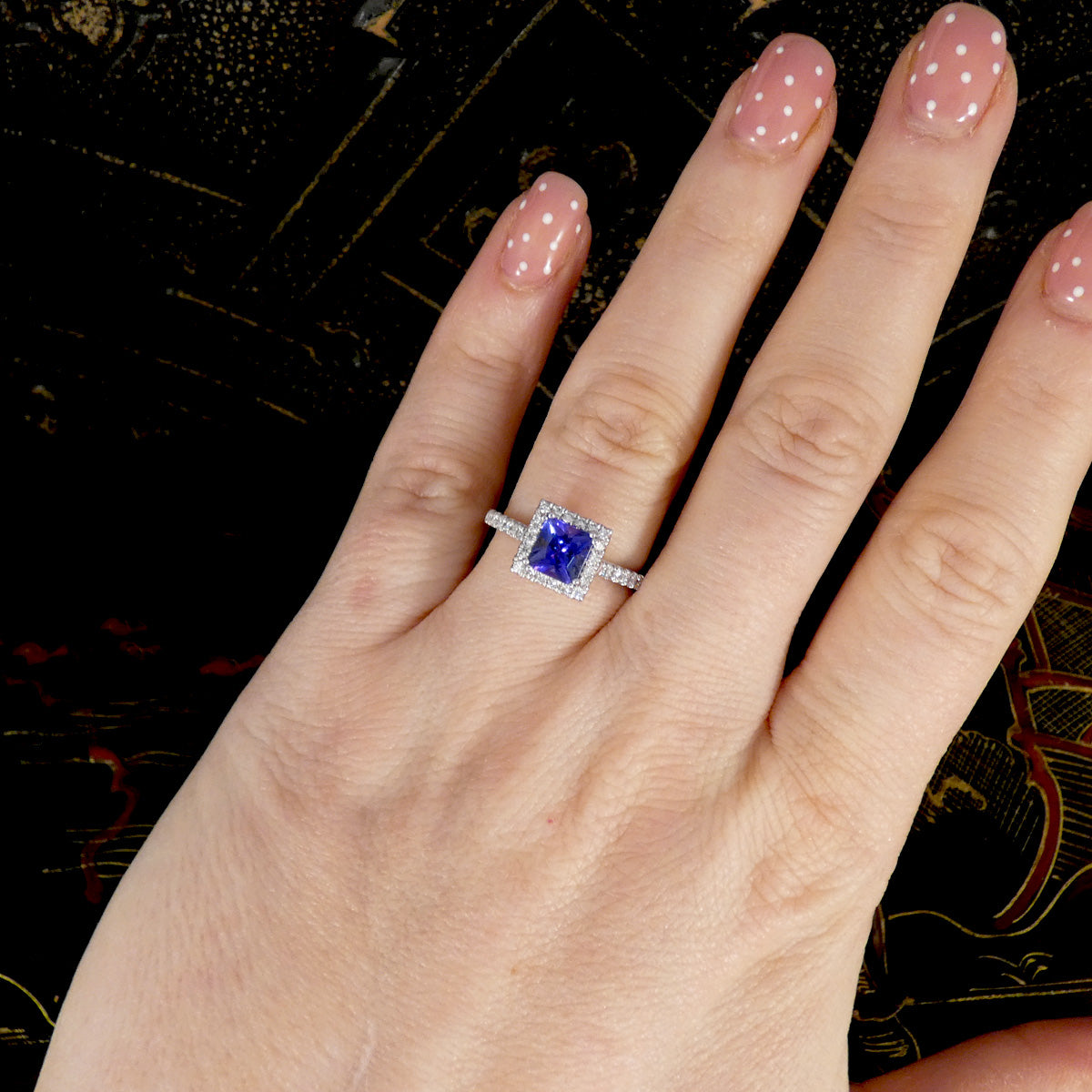 Hand wearing a ring with a blue gemstone on a dark background
