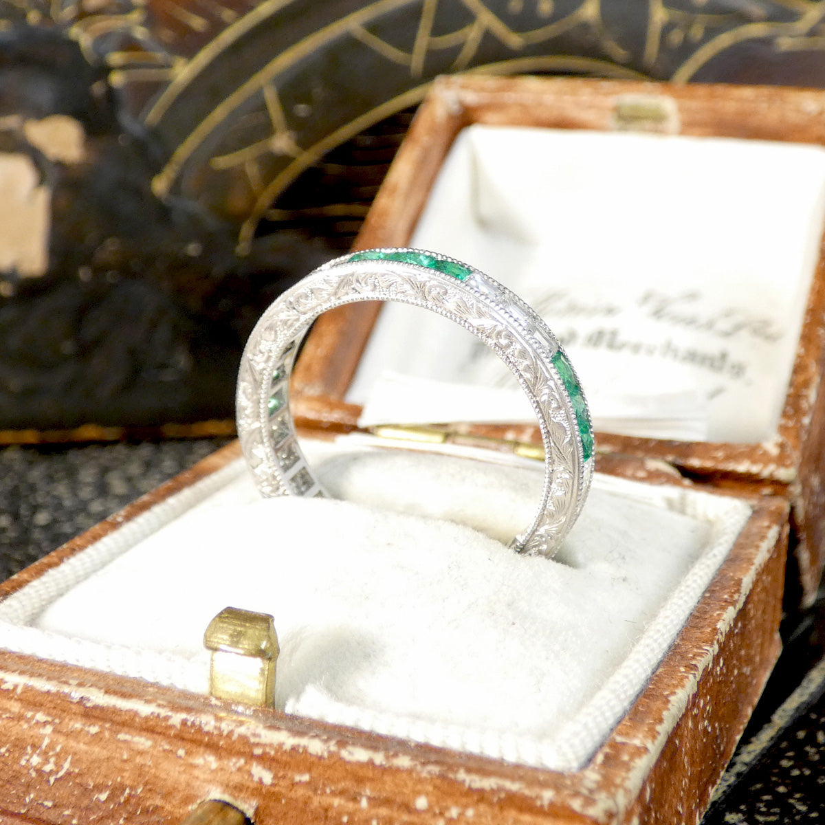Art Deco Inspired Emerald and Diamond Full Eternity Ring in Platinum displayed from the side in a vintage box.