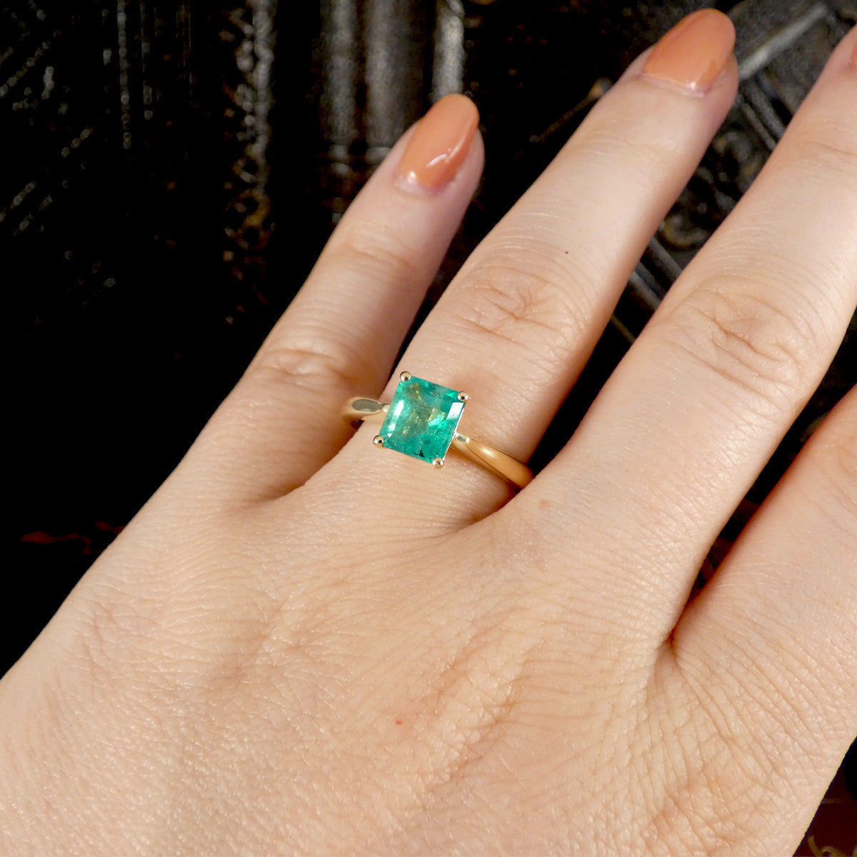 Hand wearing a gold ring with a green Emerald gemstone against a dark background
