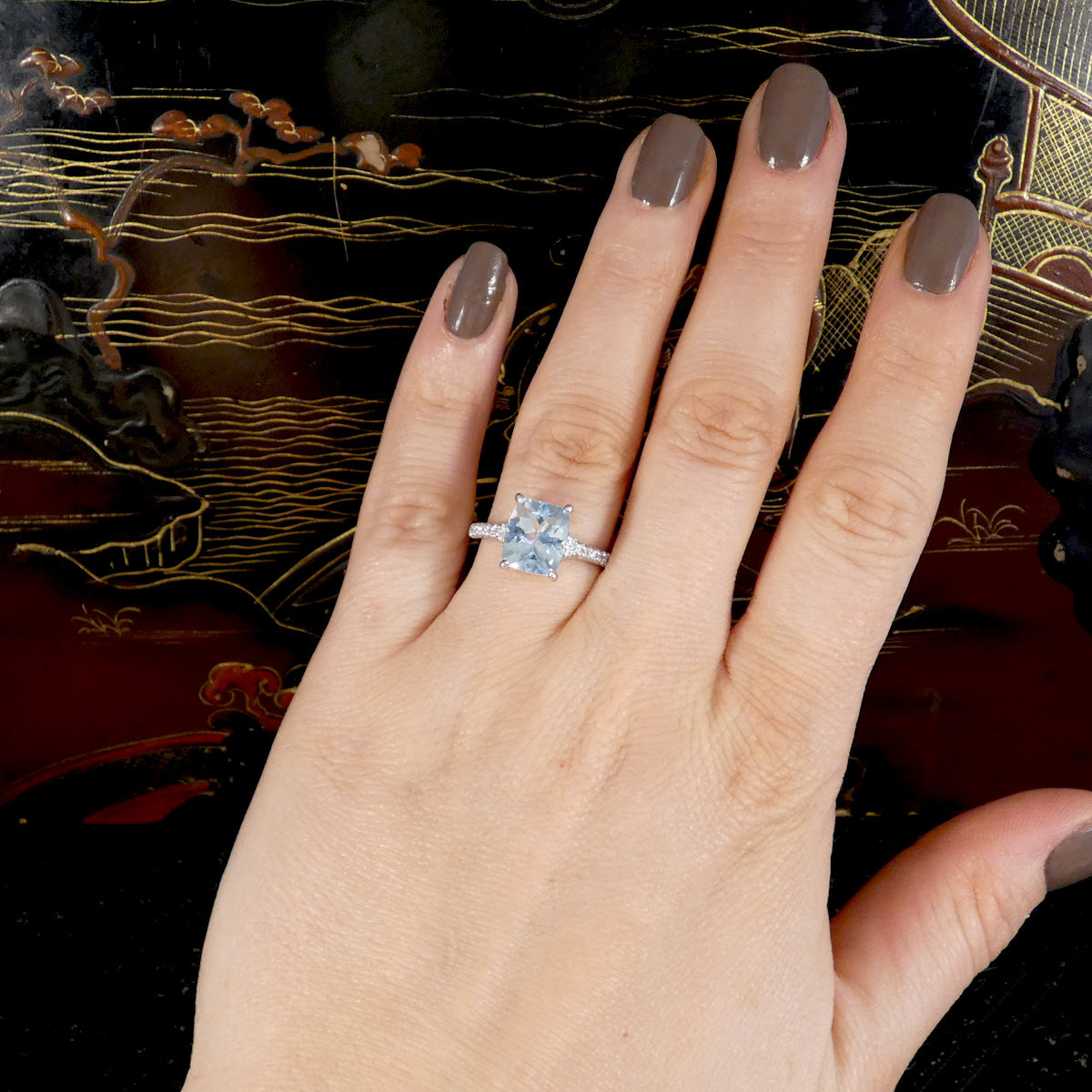 Hand wearing a aquamarine and diamond ring with a decorative background