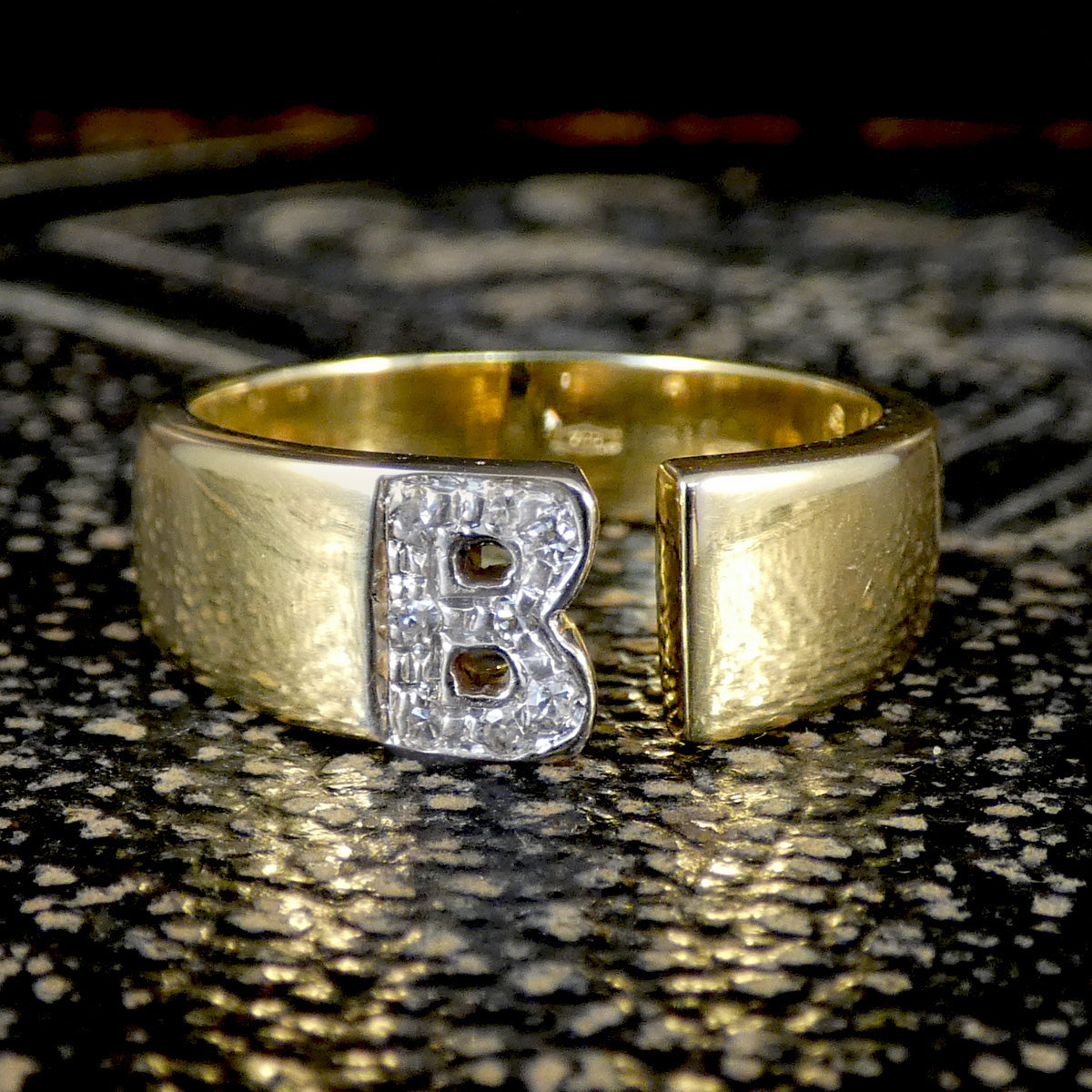 Gold ring with a diamond set 'B' on a textured surface