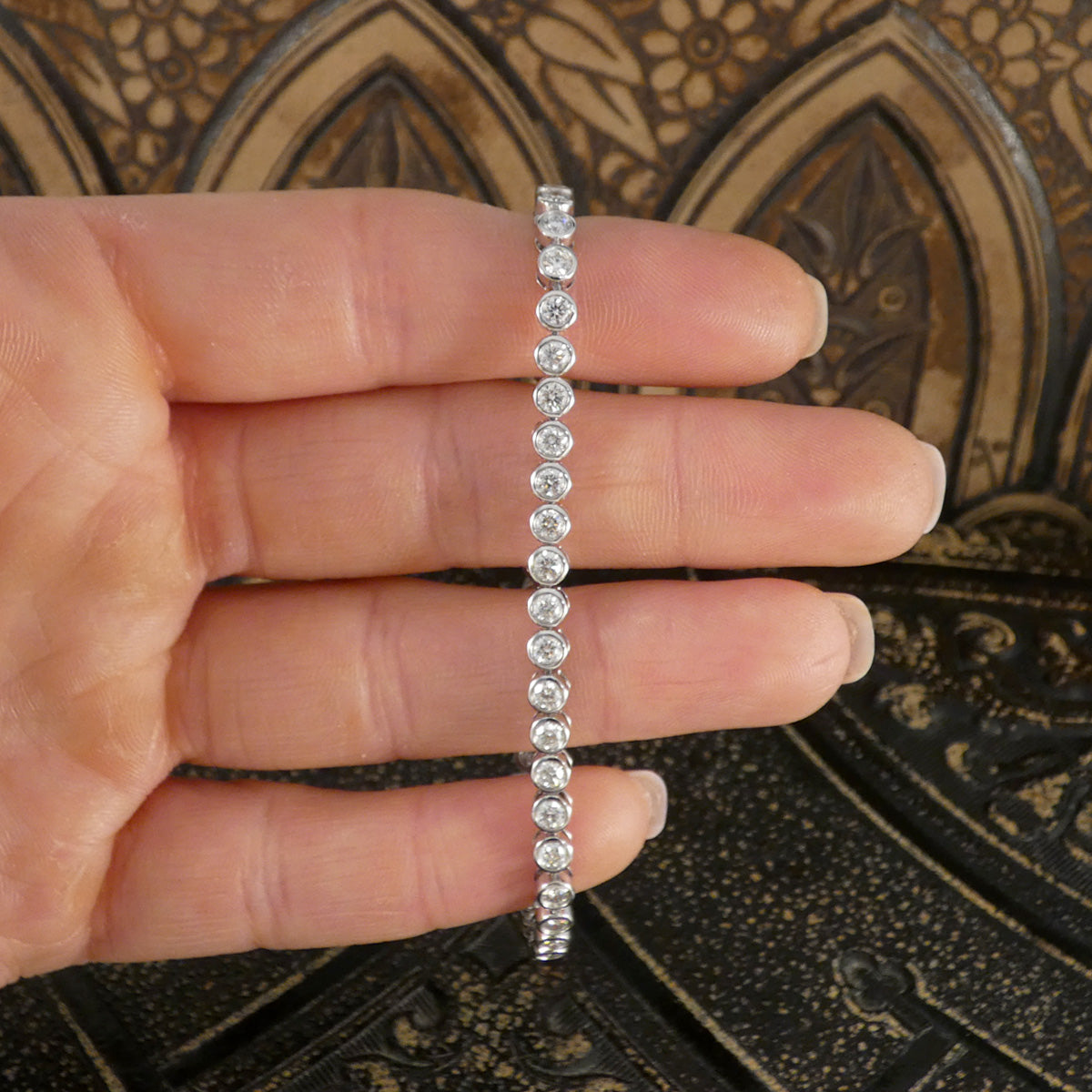A diamond tennis bracelet in a bezel setting in Platinum show on a hand