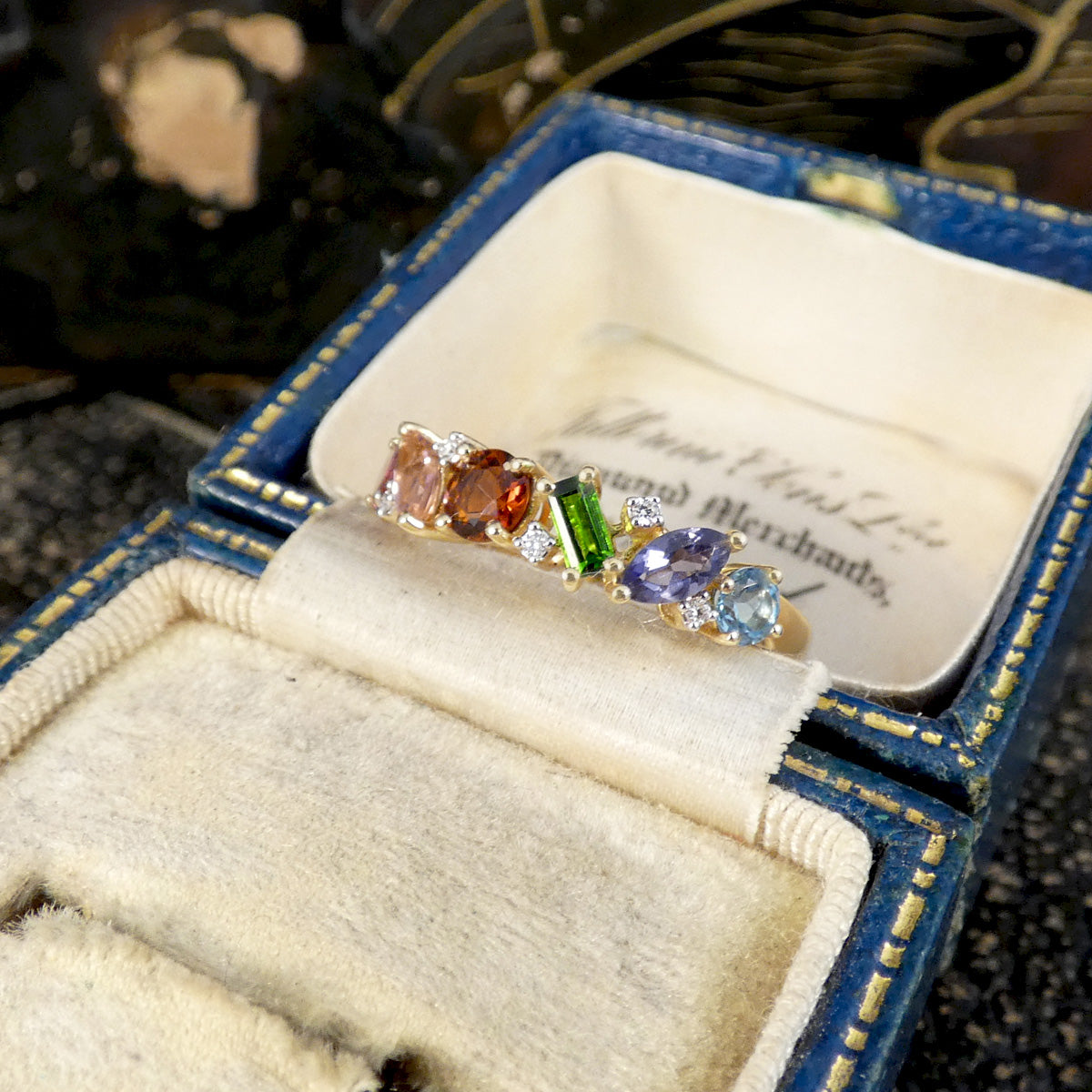 Jewelry box with a ring featuring multicolored gemstones on a textured surface.