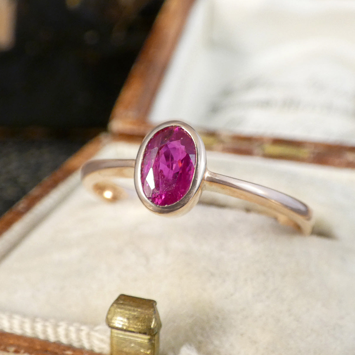 A rose gold ring with an oval-cut pink gemstone, displayed in an open vintage jewelry box.
