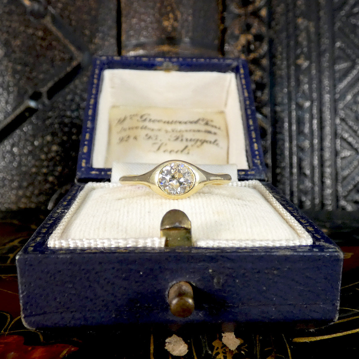 A vintage gold ring with a round diamond setting, presented inside an open dark blue velvet jewelry box with a handwritten inscription card.